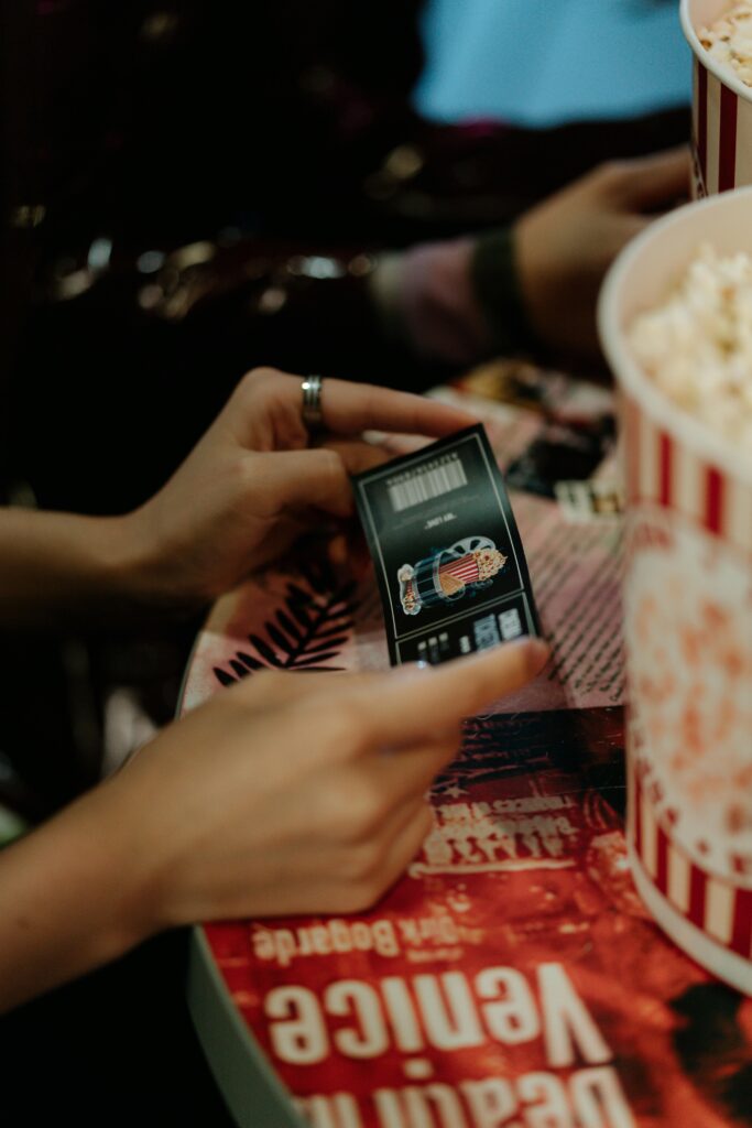 pexels photo 8261585 8261585 Close-up of hands holding a movie ticket with popcorn on a table.